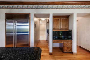 Kitchen featuring backsplash, stone counters, light wood-type flooring, and built in refrigerator. Desk/additional service counter.