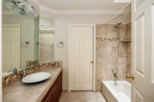 Bathroom with vanity with extensive cabinet space, molding, tiled shower / bath combo, and tile floors.