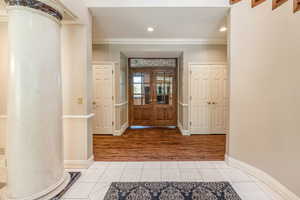 Hallway with french doors, ornamental molding, decorative columns, and hardwood flooring from off the marble flooring.