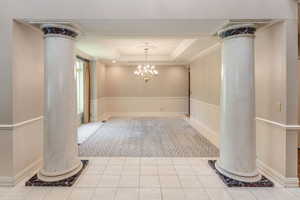 Formal Dining room with a tray ceiling, marble flooring with inlaid carpet, ornate columns, and an crystal chandelier.