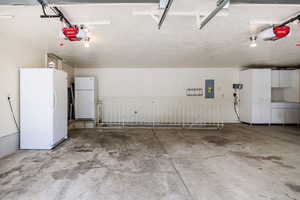 Garage with white refrigerator and a garage door opener. Cabinets included. Staircase to basement entrance, into storage/exercise room.