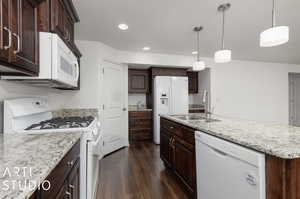 Kitchen featuring a center island with sink, white appliances, pendant lighting, and sink in island