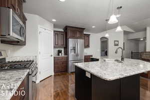 Kitchen featuring decorative light fixtures, a kitchen island with sink, dark wood-type flooring, appliances with stainless steel finishes, and sink