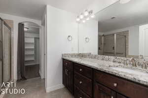 Bathroom with a shower with shower door, double sink vanity, and tile floors