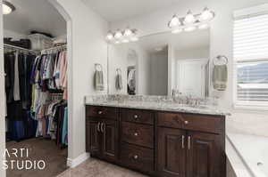 Bathroom featuring dual sinks, a healthy amount of sunlight, vanity with extensive cabinet space, and a bathing tub