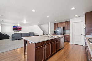 Kitchen with a textured ceiling, stainless steel appliances, a kitchen island with sink, sink, and light colored carpet