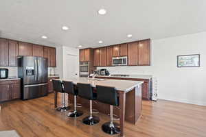 Kitchen featuring a kitchen breakfast bar, a kitchen island with sink, wood-type flooring, and stainless steel appliances