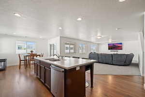 Kitchen with dishwasher, hardwood / wood-style flooring, a kitchen island with sink, sink, and a textured ceiling