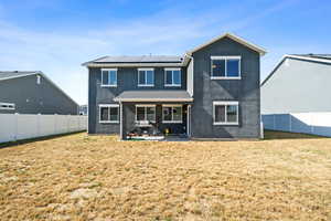 Rear view of house with a patio, solar panels, and a lawn