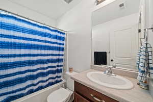 Full bathroom with shower / bath combo with shower curtain, toilet, and vanity with extensive cabinet space