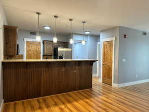 Kitchen featuring kitchen peninsula, hanging light fixtures, stainless steel refrigerator with ice dispenser, a breakfast bar, and light hardwood / wood-style floors