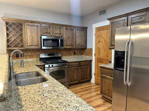 Kitchen with backsplash, light hardwood / wood-style flooring, light stone countertops, stainless steel appliances, and sink