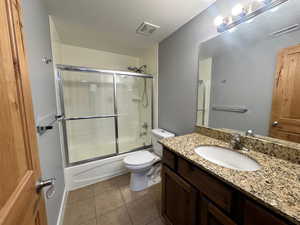 Full bathroom with tile patterned floors, toilet, combined bath / shower with glass door, vanity, and a textured ceiling