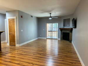 Unfurnished living room with hardwood / wood-style floors, ceiling fan, and a tiled fireplace