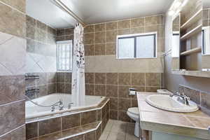 Bathroom featuring tile walls, toilet, tile flooring, tiled bath, and vanity