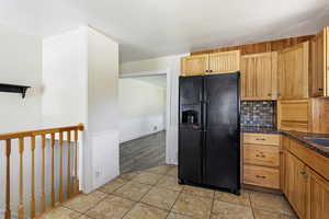 Kitchen featuring black fridge, light hardwood / wood-style flooring, tasteful backsplash, and dark stone countertops