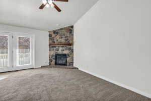 Unfurnished living room with light colored carpet, ceiling fan, vaulted ceiling, and a fireplace