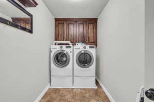 Laundry area with washing machine and clothes dryer, cabinets, and a textured ceiling