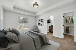 Carpeted bedroom with ensuite bathroom, a walk in closet, a closet, a raised ceiling, and a textured ceiling