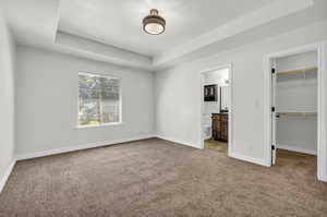 Unfurnished bedroom featuring light carpet, a closet, a tray ceiling, a walk in closet, and ensuite bathroom