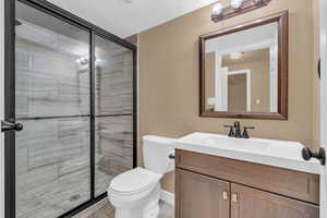 Bathroom featuring a textured ceiling, vanity, toilet, and a shower with shower door