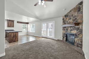 Unfurnished living room with a fireplace, light carpet, a textured ceiling, ceiling fan, and lofted ceiling