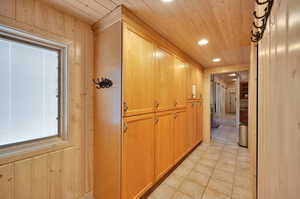 Hallway featuring light tile floors, wooden ceiling, and wood walls