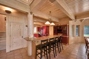 Kitchen with beamed ceiling, a breakfast bar area, decorative light fixtures, wood walls, and light tile floors