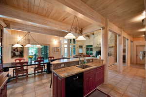 Kitchen featuring light stone countertops, beam ceiling, dishwasher, hanging light fixtures, and sink