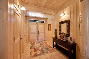 Hallway featuring wood walls, beamed ceiling, light tile flooring, and wood ceiling