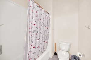 Bathroom with tile flooring, shower / bath combination with curtain, and toilet