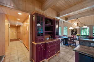 Kitchen featuring beam ceiling, hanging light fixtures, light tile flooring, and wooden walls