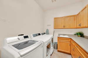 Laundry room with cabinets, sink, light tile floors, and washing machine and clothes dryer