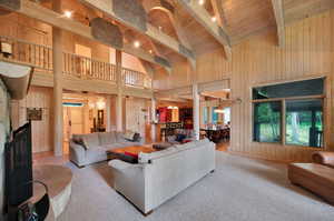 Carpeted living room featuring high vaulted ceiling, wood walls, beamed ceiling, and wood ceiling