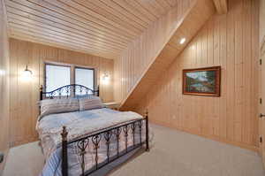 Carpeted bedroom featuring wood walls, vaulted ceiling with beams, and wooden ceiling