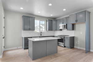 Kitchen with gray cabinets, tasteful backsplash, stainless steel appliances, a kitchen island, and light hardwood / wood-style flooring