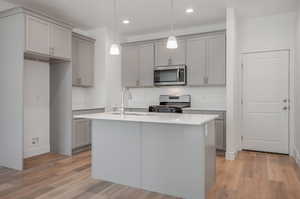 Kitchen with light hardwood / wood-style floors, a kitchen island with sink, appliances with stainless steel finishes, sink, and pendant lighting