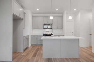 Kitchen with a kitchen island with sink, pendant lighting, range, and light hardwood / wood-style flooring