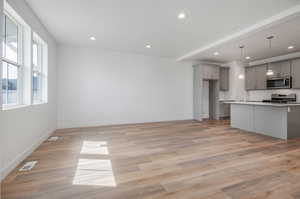 Kitchen with an island with sink, gray cabinetry, light hardwood / wood-style flooring, and stove