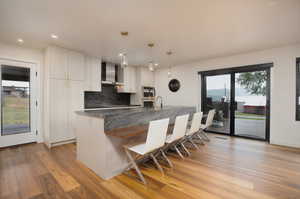 Kitchen with wall chimney exhaust hood, light hardwood / wood-style floors, and backsplash