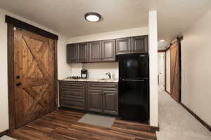 Kitchen featuring light stone countertops, dark carpet, a barn door, black refrigerator, and sink