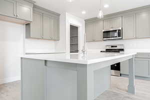 Kitchen featuring light hardwood / wood-style flooring, stainless steel appliances, hanging light fixtures, and gray cabinetry
