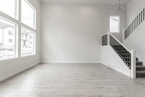 Unfurnished living room with an inviting chandelier, a high ceiling, and light wood-type flooring