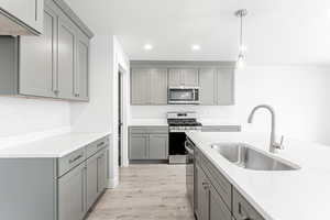 Kitchen featuring gray cabinetry, appliances with stainless steel finishes, sink, pendant lighting, and light hardwood / wood-style flooring