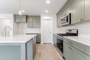 Kitchen with appliances with stainless steel finishes, sink, light wood-type flooring, and decorative light fixtures