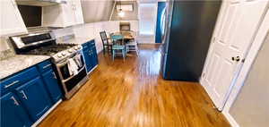 Kitchen featuring light hardwood / wood-style floors, stainless steel range with gas stovetop, blue cabinets, white cabinetry, and refrigerator