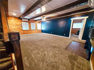 Interior space featuring beamed ceiling, carpet flooring, wooden walls, and ceiling fan