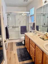 Bathroom featuring dual vanity, walk in shower, hardwood / wood-style flooring, and toilet