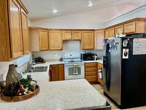 Kitchen with white electric range, stainless steel fridge, light wood-type flooring, sink, and lofted ceiling