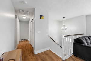 Hallway with a textured ceiling, a notable chandelier, and hardwood / wood-style floors